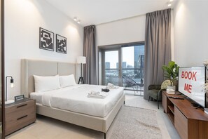 Une chambre d’hôtel moderne dotée d’un grand lit, d’un bureau avec un ordinateur, d’une télévision et d’un balcon offrant une vue sur la ville.
