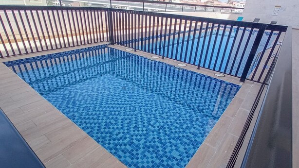 Ein rechteckiger Swimmingpool mit blauen Fliesen, umgeben von einem schwarzen Metallgeländer.