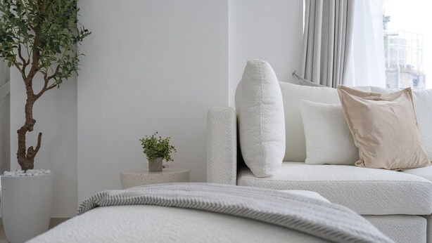 Un dormitori minimalista amb un sofà blanc, una petita taula de nit amb una planta, i un finestral gran amb cortines.