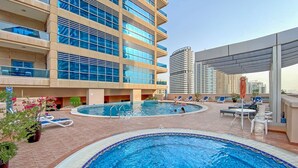 A rooftop swimming pool with lounge chairs and a modern building in the background. - Classy 1-bedroom Apartment in Dubai Marina With City Views (Dubai)