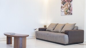 A modern living room with a grey sofa, two wooden side tables, and a wall-mounted lamp. - Spacious 3-bedroom With Comfortable Living Area in Dubai Marina (Dubai)