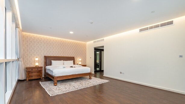 A modern bedroom with a wooden bed, a nightstand, a patterned wall, and a large window. - Spacious 3-bedroom With Comfortable Living Area in Dubai Marina (Dubai)