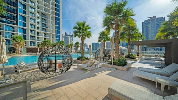 A rooftop pool area with lounge chairs, palm trees, and a spherical decorative structure.