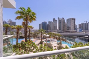 A rooftop pool area with palm trees, a view of a city skyline, and high-rise buildings in the background.