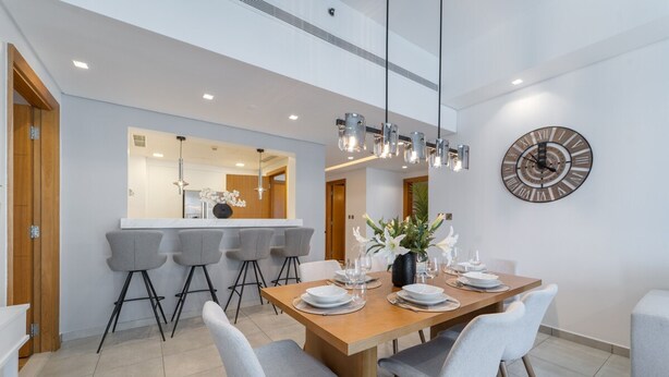Un espace repas moderne avec une table en bois dressée pour quatre personnes, des chaises grises et une grande horloge murale.