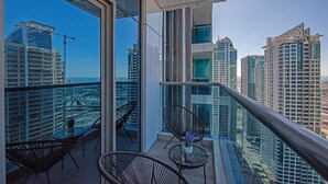 A balcony with a glass railing, two chairs, and a small table with a vase. - Warm 1-bedroom Family-friendly Aparment in JLT (Dubai)