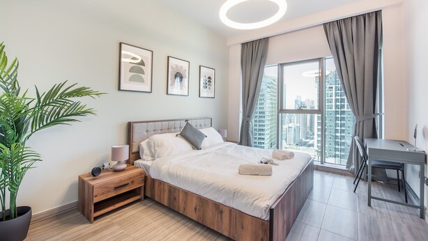 A modern bedroom with a wooden bed, bedside tables, a desk, and a large window with curtains. - Warm 1-bedroom Family-friendly Aparment in JLT (Dubai)