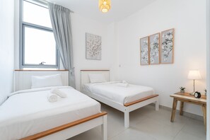 Hotellihuone, jossa on kaksi erillistä sänkyä, yöpöytä lampulla ja ikkuna, jossa on verhot.