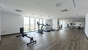 A spacious gym with cardio machines, weightlifting equipment, and large windows offering a view of the outdoors. - Elegant 2-bedroom Apartment in Dubai South Close to Expo 2020 (Dubai)