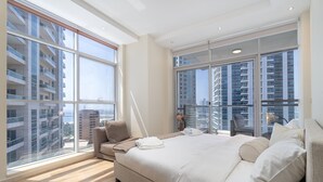 A modern bedroom with a large bed, a sofa, and a view of high-rise buildings through floor-to-ceiling windows. - Bright 1-bedroom With View Dubai Marina (Dubai)