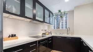 A modern kitchen with black cabinets, a white countertop, and a window with a view of buildings. - Bright 1-bedroom With View Dubai Marina (Dubai)