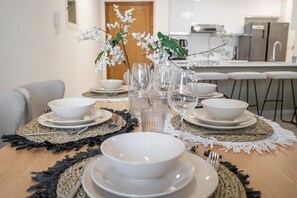 A dining table set with white bowls, plates, and cutlery, surrounded by woven placemats and a vase with white flowers. - Restful 1-bedroom Apartment at Al Andalus in Jumeirah Golf Estates (Dubai)