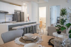 A modern kitchen with a central island, bar stools, and a dining area with a table set for two. - Restful 1-bedroom Apartment at Al Andalus in Jumeirah Golf Estates (Dubai)