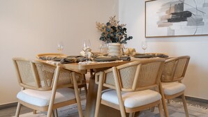 A dining area with a round table set for six, surrounded by wicker chairs with cushions. - Boho-inspired 1 bed in Production City (Dubai)