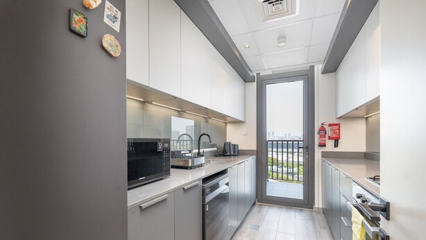 A modern kitchen with stainless steel appliances, a built-in oven, and a large window overlooking a cityscape. - Boho-inspired 1 bed in Production City (Dubai)