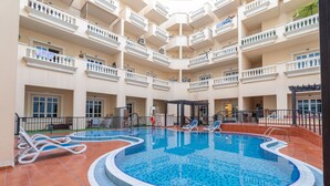 Un hotel de varios pisos con piscina central, balcones y una zona de estar techada.