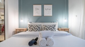 Una cama bien hecha con toallas enrolladas y un masajeador, dos cuadros en la pared y mesitas de noche con lámparas.