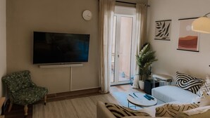 Una sala de estar con una televisión de pantalla plana, un sofá, una silla, una mesita de centro y una planta en maceta.