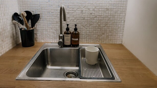 Una cocina con un lavamanos de acero inoxidable, encimera de madera y salpicadero de azulejos.