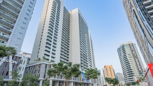 A modern high-rise building with a prominent 'SON' sign, surrounded by other tall buildings and greenery. - Bali-inspired 1-bedroom Apartment for 4 in Business Bay (Dubai)