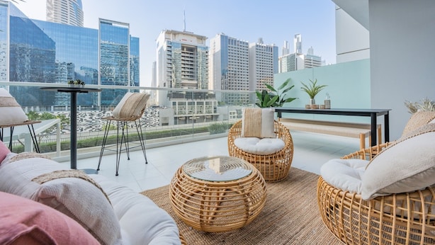 A balcony with wicker furniture, a table, and a view of city buildings. - Bali-inspired 1-bedroom Apartment for 4 in Business Bay (Dubai)