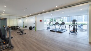 A modern gym with cardio machines, weightlifting equipment, and a large mirror. - Bali-inspired 1-bedroom Apartment for 4 in Business Bay (Dubai)
