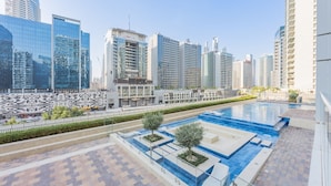 A modern urban setting with high-rise buildings, a swimming pool, and a landscaped area with trees. - Bali-inspired 1-bedroom Apartment for 4 in Business Bay (Dubai)