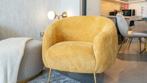 Een moderne woonkamer met een geel fauteuil, een grijze bank en een eethoek met een witte stoel en een tafel.