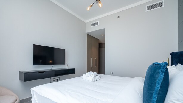 Een moderne hotelkamer met een groot bed, een flatscreen televisie aan de muur, een donkere houten garderobe en een blauw sierkussen.