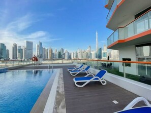 Una piscina en la azotea con sillones de descanso y vistas al horizonte de la ciudad.