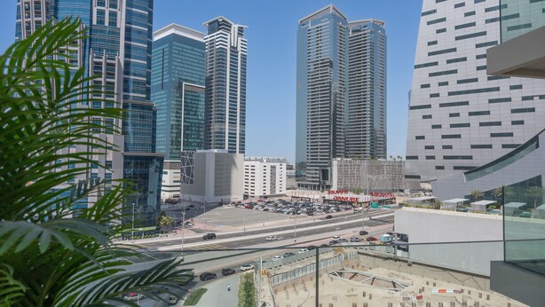 A cityscape with modern high-rise buildings, a busy intersection, and a construction site. - Elegant 1BR in Business Bay Sleeps 4 Near Downtown (Dubai)