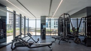 A modern gym with cardio machines, weightlifting equipment, and large windows offering views of the cityscape. - Elegant 1BR in Business Bay Sleeps 4 Near Downtown (Dubai)