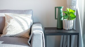 A modern living room with a grey sofa, a patterned throw pillow, a green vase, and a potted plant on a side table. - Trendy 1-bedroom Apartment With Stunning Views at MBL Residences JLT (Dubai)