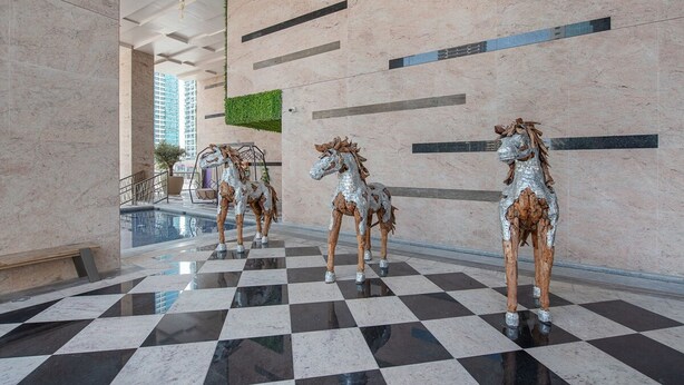 A lobby with a checkered floor, three metallic horse statues, a pool, and a green wall. - Trendy 1-bedroom Apartment With Stunning Views at MBL Residences JLT (Dubai)
