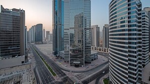 A modern urban area with high-rise buildings, a wide road, and a pedestrian walkway. - Cozy Studio Apartment Perfect for 2 in Business Bay (Dubai)