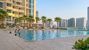 A swimming pool with lounge chairs and palm trees, surrounded by high-rise buildings. - Cozy Studio Apartment Perfect for 2 in Business Bay (Dubai)