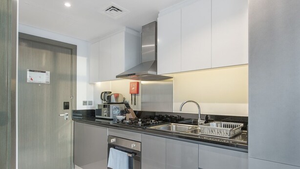 A modern kitchen with stainless steel appliances, a built-in oven, and a large sink. - Cozy Studio Apartment Perfect for 2 in Business Bay (Dubai)