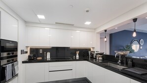 Una cocina moderna con armarios blancos, encimeras negras y electrodomésticos de acero inoxidable.