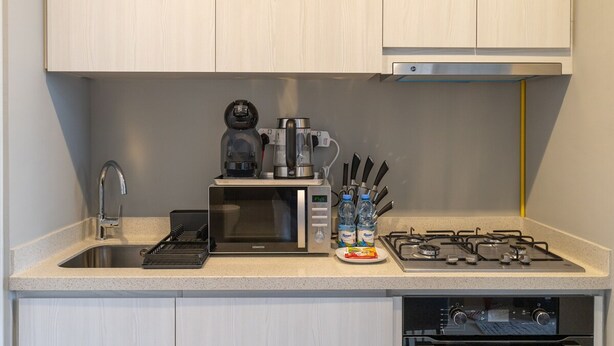A modern kitchen with a built-in microwave, coffee maker, gas stove, and a sink. - Stylish 1-bedroom Apartment With Stunning Canal Views at Business Bay (Dubai)