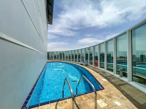 A rooftop swimming pool with clear blue water, a lifebuoy, and a view of the city skyline.