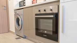 A compact kitchen with a washing machine, oven, and microwave. - Immaculate Studio Great for 2 in Meydan (Dubai)