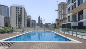 A rooftop swimming pool with a wooden deck, surrounded by high-rise buildings and construction cranes. - Immaculate Studio Great for 2 in Meydan (Dubai)