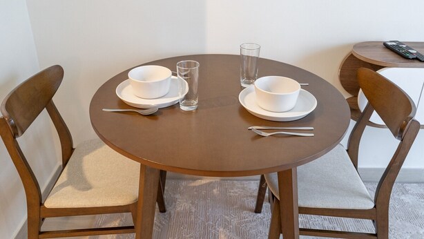A round dining table with two white bowls, two spoons, and two glasses. - Immaculate Studio Great for 2 in Meydan (Dubai)