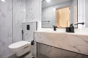 A modern bathroom with a white toilet, a large mirror, and a marble backsplash. - Elegant 1-bedroom Apartment in Jumeirah Village Triangle With Balcony Bliss (Dubai)