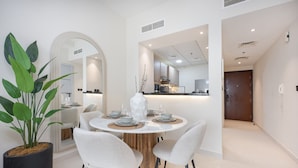A modern dining area with a round table, white chairs, and a potted plant. - Elegant 1-bedroom Apartment in Jumeirah Village Triangle With Balcony Bliss (Dubai)