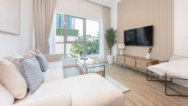 A modern living room with a sofa, a coffee table, a TV, and a view of the city. - Stylish 1BR Urban Living in Dubai Marina (Dubai)
