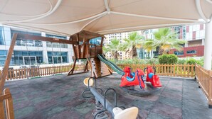 A playground with a seesaw, a slide, and a climbing structure. - Stylish 1BR Urban Living in Dubai Marina (Dubai)