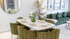 A dining table set with white plates, gold cutlery, and a green vase with flowers. - Modern 2BR Apartment Perfect for 4 in Business Bay (Dubai)