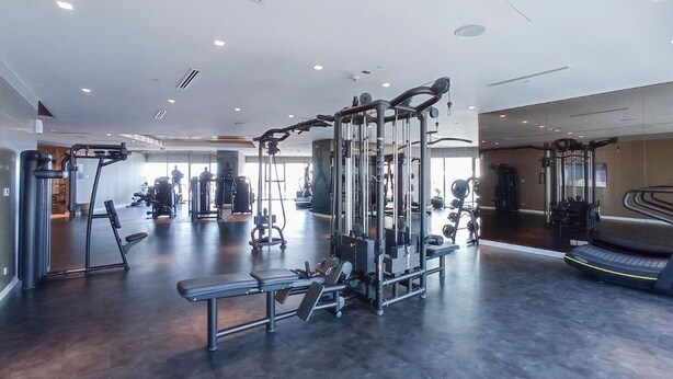 A modern gym with various exercise equipment, a bench, and a treadmill. - Modern 2BR Apartment Perfect for 4 in Business Bay (Dubai)