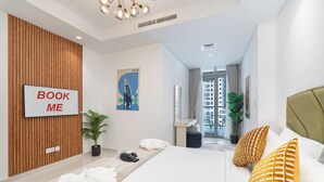 A modern hotel room with a large bed, a TV mounted on the wall, a wooden panel wall, and a view of the city through the window. - Modern 2BR Apartment Perfect for 4 in Business Bay (Dubai)
